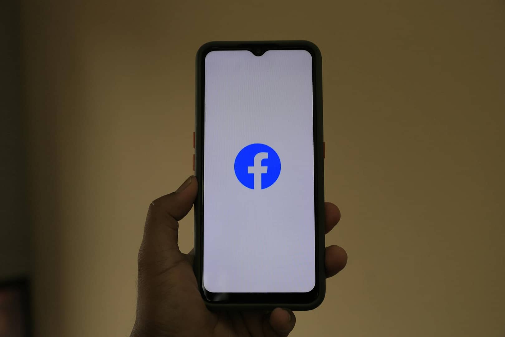 A smartphone held in hand showing the Facebook logo on its screen.